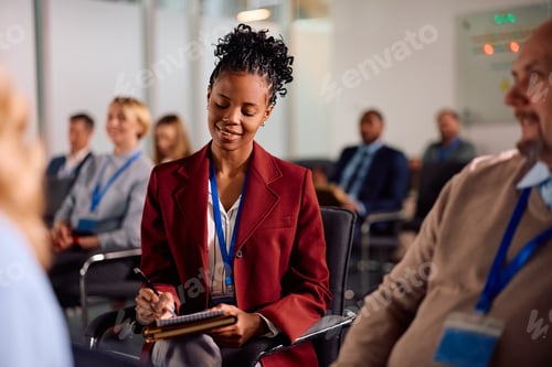 Preview: Black businesswoman taking notes during seminar at convention center.
