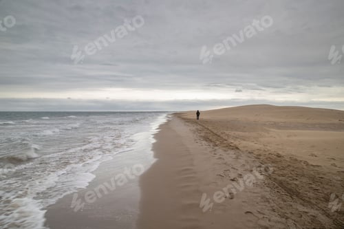 Preview: Man walking along the coastline under the cloudy sky