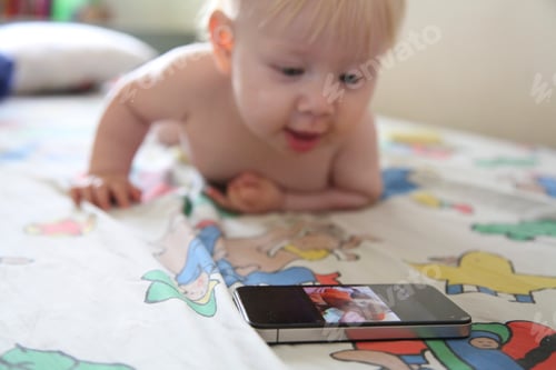 Preview: Baby plays with smartphone on bed