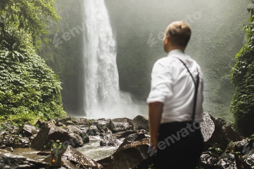 Preview: Traveller man looking on huge waterfall Nung-Nung in Bali Jungle. Asia travel concept. Amazing view.