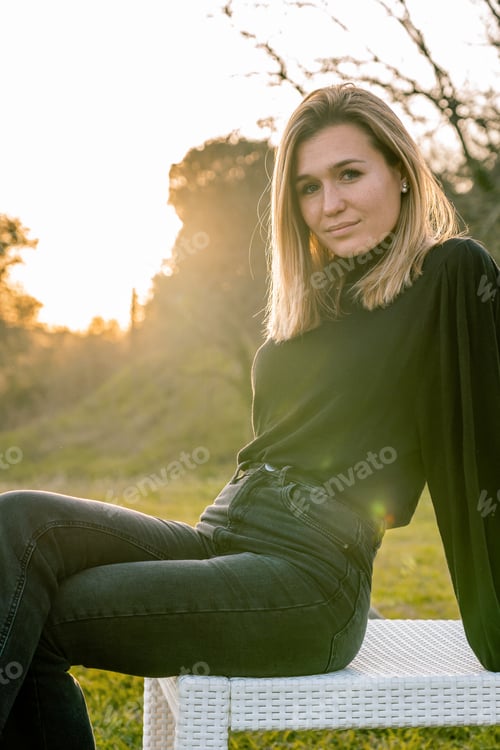 Preview: Portrait of a young blonde-haired model dressed in black looking at the camera sitting cross-legged