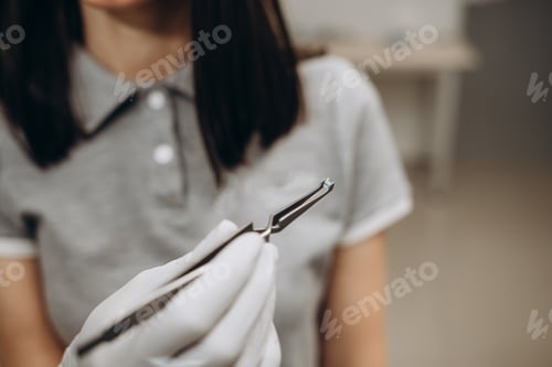 Preview: the orthodontist takes the button for braces with forceps.