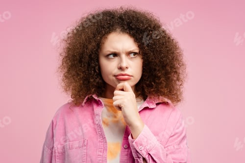 Preview: Serious woman with curly hair looking away, choosing something, standing isolated on pink background