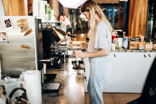 Preview: A young beautiful thin blonde,dressed in casual outfit,is cooking coffee in a popular coffee shop