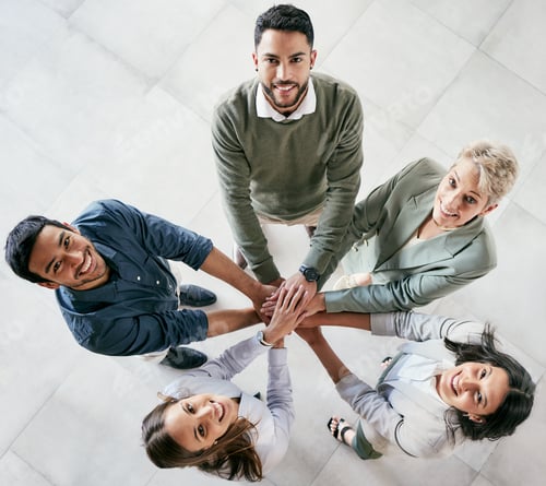 Preview: High angle shot of a group of young businesspeople joining hands in solidarity in a modern office