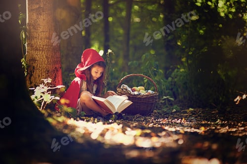Preview: Shot of a little girl in a red cape reading a book in the woods