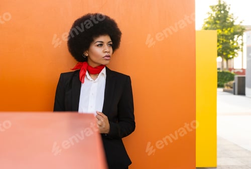 Preview: Confident black woman in formal outfit standing near colorful wall
