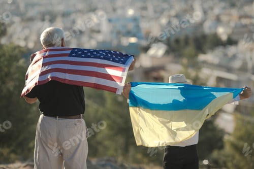 Preview: Retired man and kid boy holding the flags of the USA and Ukraine on city view