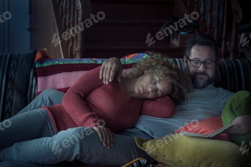 Preview: Couple relax at home by night with woman sleeping and man reading a book
