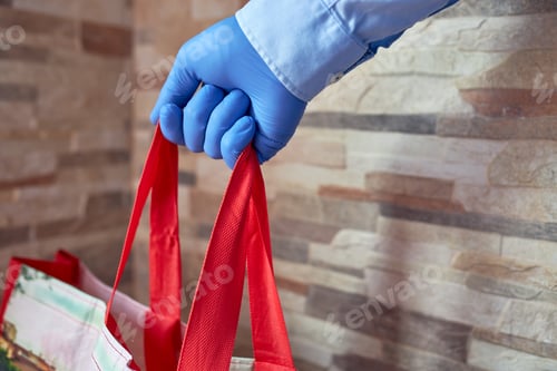 Preview: Hand with a latex glove holding a reusable shopping bag
