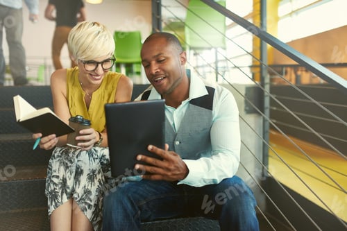 Preview: Two creative millenial small business owners working on social media strategy sitting in staircase