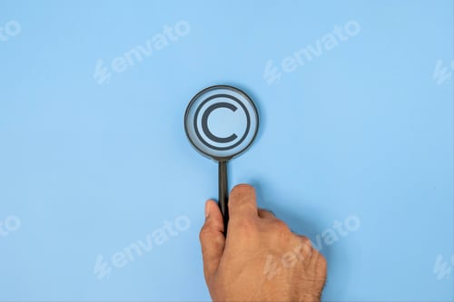 Preview: Close-up of a hand holding a magnifying glass focusing on a copyright symbol.