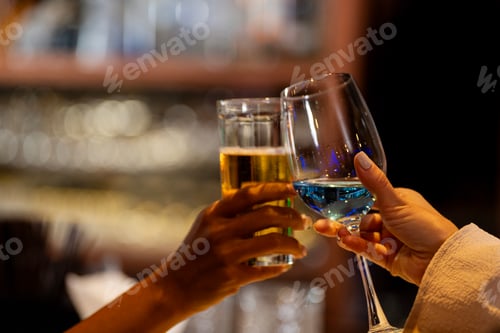 Preview: Close-up of two female friends toasting and clinking glasses of wine and beer