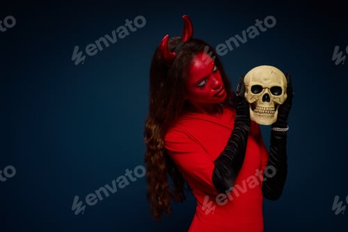 Preview: A captivating woman dressed in a devil costume holds a skull, celebrating Halloween festivities