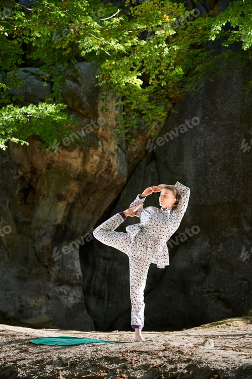 Preview: Woman practicing yoga outdoors in forest. Barefoot female on yoga mat surrounded by trees and rocks