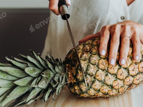 Preview: Blonde woman with green eyes in modern kitchen and about to prepare a pineapple