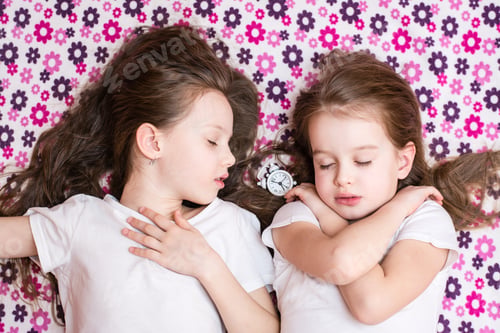 Preview: Two sleeping girls and a white alarm clock in between. Top view