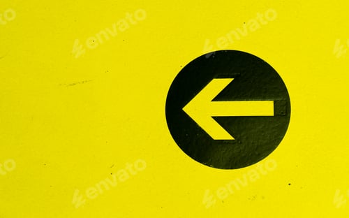 Preview: Arrow on a black circle isolated on a yellow wall showing direction