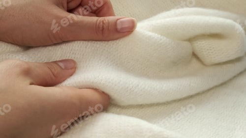 Preview: female's hand on the fabric of white plush cloth with soft nap. Clothing industry concept, slow