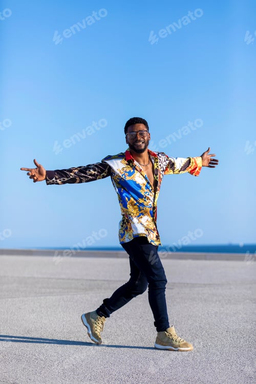 Preview: Front view of an african american man standing outdoors while arms raised in sunny day