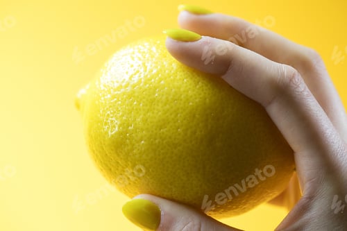 Preview: Hand with yellow painted nails holding a fresh lemon