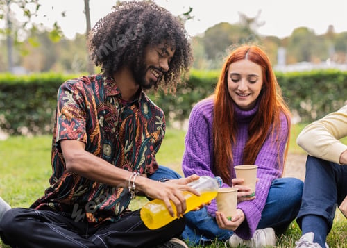 Preview: Multiracial friends sharing refreshment sitting on grass in park