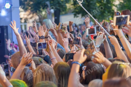Preview: Teenagers at the concert, hands up, using mobile devices, crowd cheering up for an artist on stage