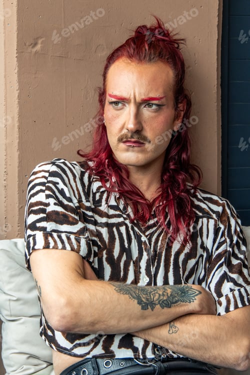 Preview: Non-binary person with red hair and mustache wearing zebra shirt and showing tattoos