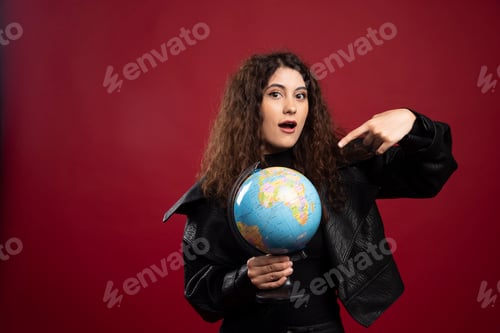 Preview: Cheerful woman pointing at globe over red background