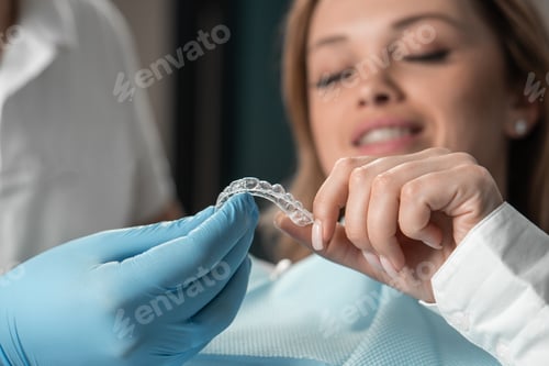 Preview: Attentive dentist demonstrating aligner aligner in hands, showing female patient in dental office
