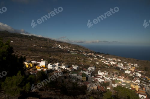 Preview: Hill covered in buildings and greenery with the sea under a blue sky on the background
