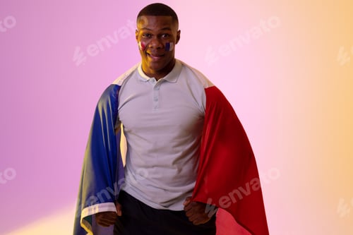 Preview: Portrait of happy african american male supporter with flag of france over pink lighting