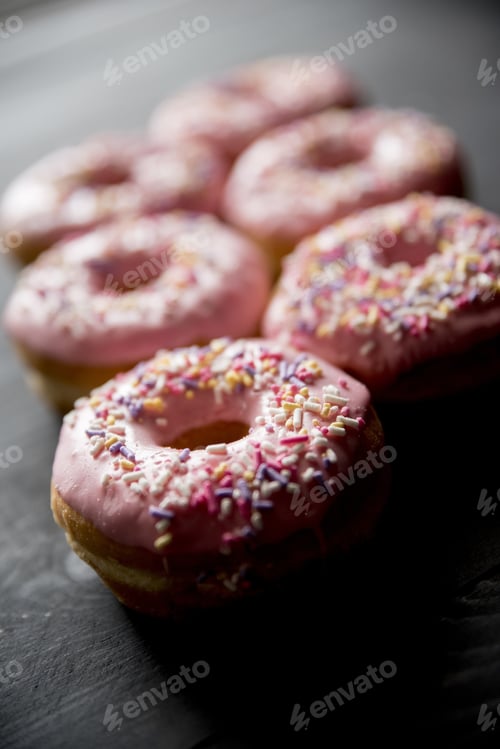 Preview: Vertical closeup shot of pink donuts with sparkles and a blurred background