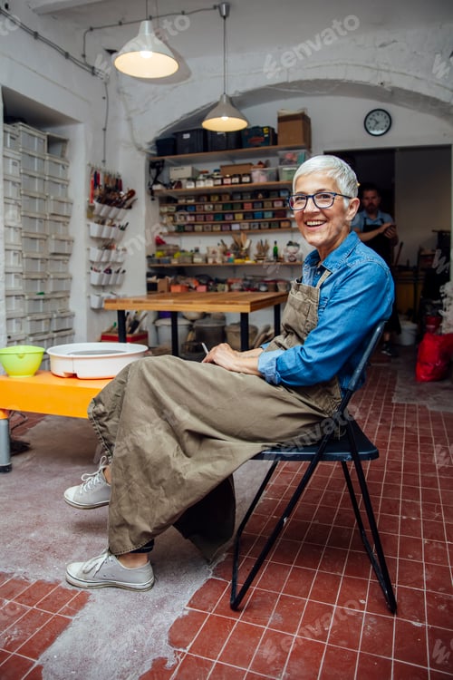 Preview: Senior woman sitting on chair, smoking and relaxing in pottery workshop