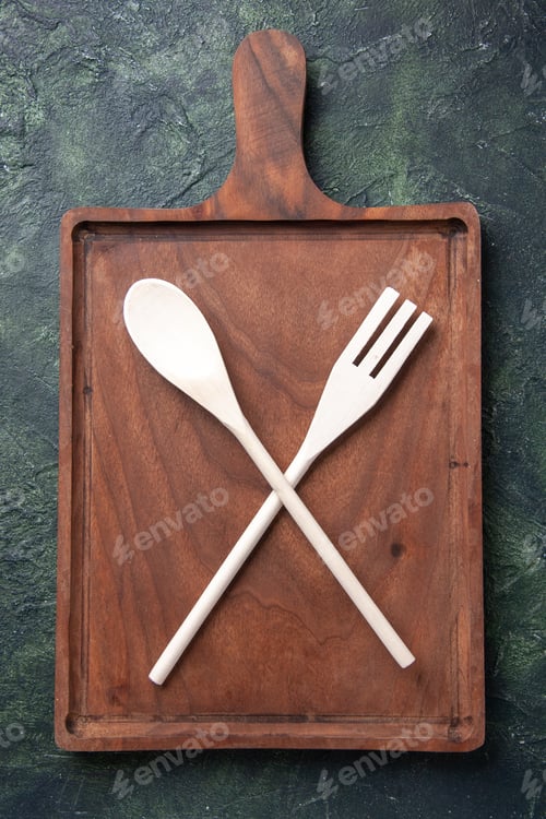Preview: top view plastic utencils fork and spoon inside wooden cutting board on dark background knife