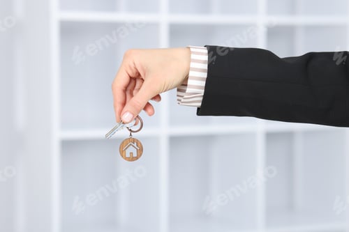 Preview: Real estate agent holding key with house shaped keychain indoors, closeup