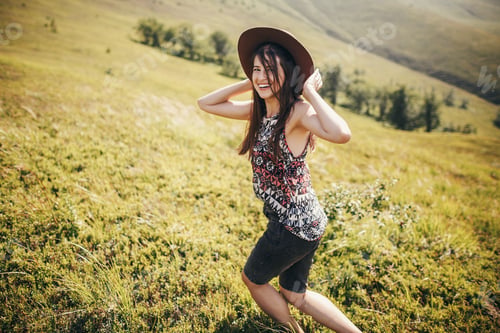Preview: Traveler hipster girl in hat, walking in sunny mountains