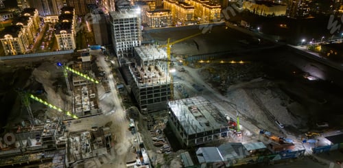 Preview: Large building under construction at night with cranes and workers