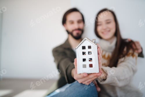 Preview: Young couple owners holding house model, moving in, new home and relocation concept.