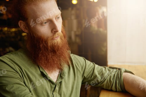 Preview: Cropped portrait of Caucasian hipster male having long beard and blue eyes sitting at coffee shop de
