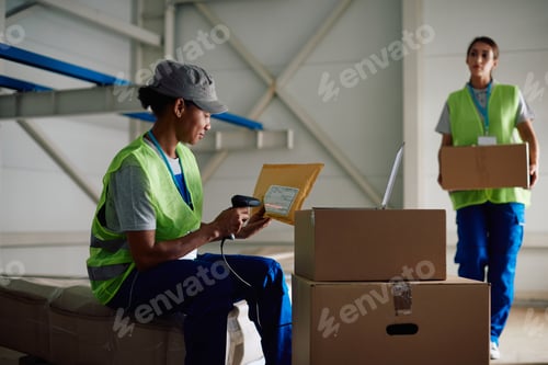 Preview: Smiling female warehouse worker scanning packages while working at storage compartment.