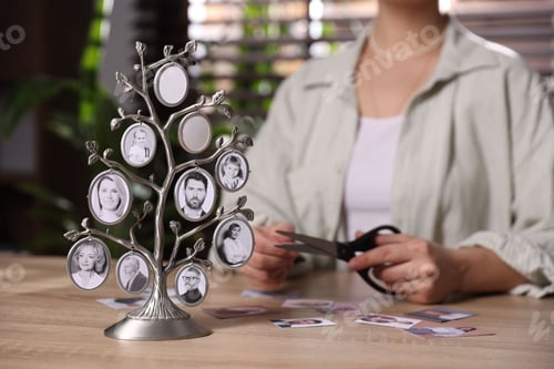 Preview: Woman cutting out pictures of her relatives at table indoors, focus on family tree photo frame