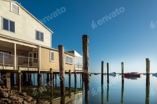 Preview: Serene waterfront scene with a house on stilts and boats on calm water under a clear blue sky