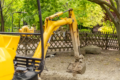 Preview: A yellow excavator is digging into the soil at a construction site surrounded by green trees