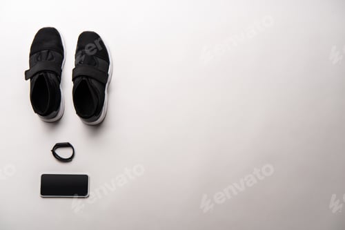 Preview: view from above of arranged black sport shoes, fitness tracker and smartphone with blank screen