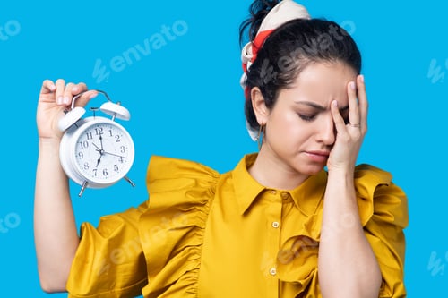 Preview: Woman in a mustard dress holding a clock and looking upset