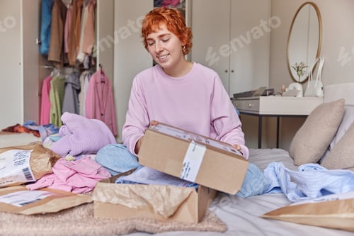 Preview: Indoor shot of happy redhead young woman holds parcel box receives order from internet store buys