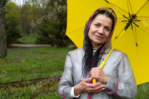 Preview: Happy senor woman in yellow raincoat enjoying life and walking in the park.