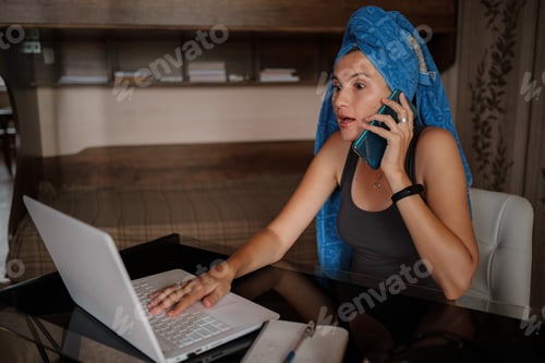 Preview: Shot of pretty young woman using her mobile phone while working with laptop sitting at home.