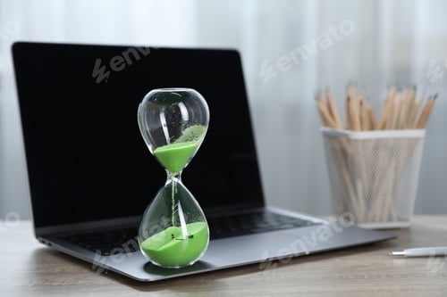 Preview: Deadline. Hourglass with flowing sand, stationery and laptop on wooden table indoors